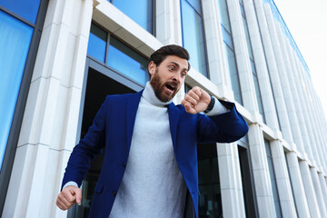 Emotional businessman looking at watch near building, low angle view. Being late concept
