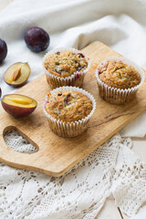 Seasonal muffins with plums and poppy seeds on white wooden and textile background close up selective focus 