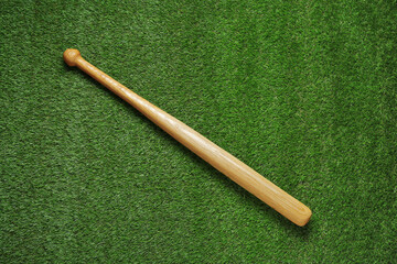 Wooden baseball bat on green grass, top view. Sports equipment