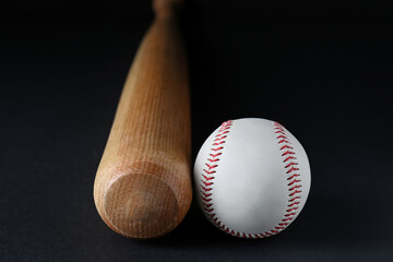 Wooden baseball bat and ball on black background, closeup. Sports equipment