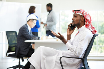 young African muslim businessman in white traditional outfit, talking on smartphone for work in the...