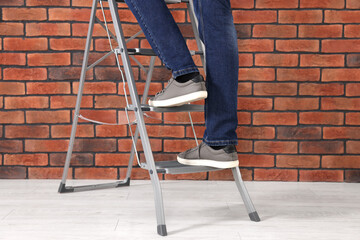 Man climbing up metal stepladder near brick wall, closeup