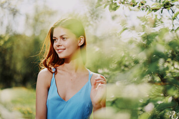 Woman smile with teeth in profile happiness in nature in the summer near a green tree in the garden of the park in a blue dress, the concept of women's health and beauty with nature sunset