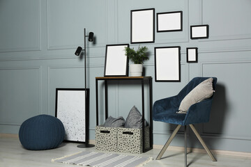 Stylish room interior with empty frames hanging on grey wall near console table