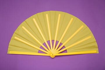 Bright yellow hand fan on purple background, top view