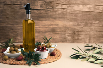Bottle of oil, olives and tree twigs on beige table, space for text