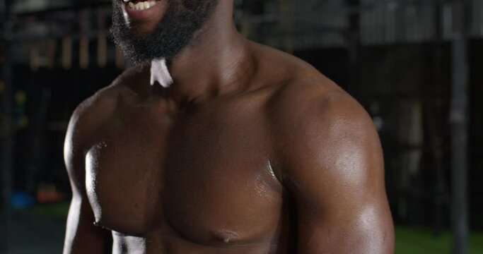 Cropped closeup of strong athletic black Afro African American beadrded smiling man with muscular sweaty torso with chest muscles body care slow motion