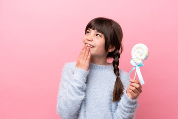 Little caucasian girl holding a lollipop looking up while smiling