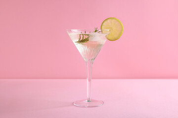 Martini glass of cocktail with lemon slice and rosemary on pink background