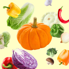 Many different fresh vegetables falling on pale light yellow background