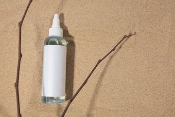 Bottle with serum and branches on sand, top view with space for text. Cosmetic product