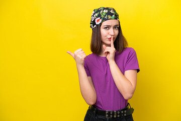 Young Ukrainian woman isolated on yellow background pointing to the side and doing silence gesture