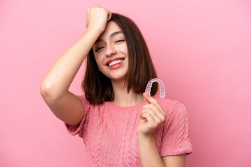 Young Ukrainian woman holding invisible braces isolated on pink background has realized something...