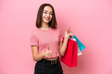 Young Ukrainian woman isolated on pink background holding shopping bags and with thumb up