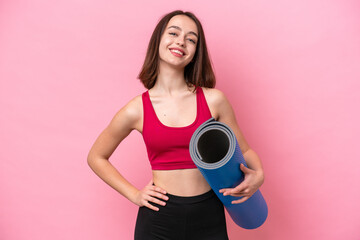 Young sport Ukrainian woman going to yoga classes while holding a mat isolated on pink background posing with arms at hip and smiling