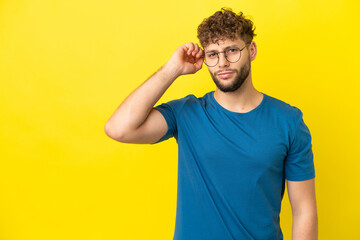 Young handsome caucasian man isolated on yellow background having doubts