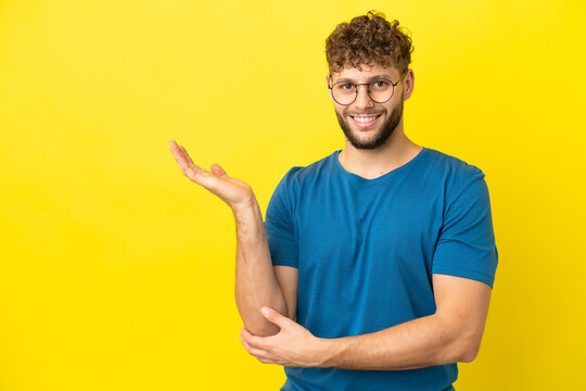 Young handsome caucasian man isolated on yellow background extending hands to the side for inviting to come