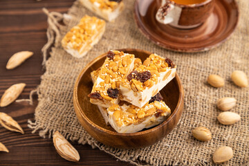Traditional candy nougat with nuts and sesame on brown wooden, side view, selective focus.