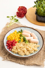 Mixed quinoa porridge, sweet corn and small sausages on white wooden, side view.