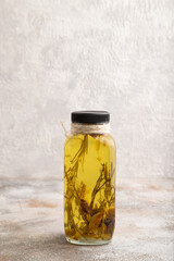 Sunflower oil in a glass jar with various herbs and spices on a brown concrete. Side view, copy space.