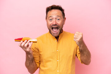 Middle age Caucasian man holding sashimi isolated on pink background celebrating a victory in...