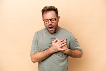 Middle age caucasian man isolated on beige background having a pain in the heart