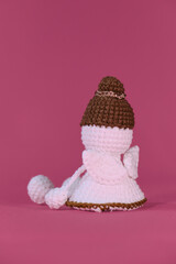 Cute little angel crocheted, handmade art. Rear view of the tiny wings. Amigurumi one white angel without face wears brown hat, sits on pink background. Soft DIY toy made of natural cotton and wool.