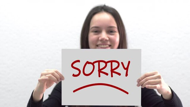 Conceptual message "Sorry" on canvas frame label hold by beautiful girl smiling at camera