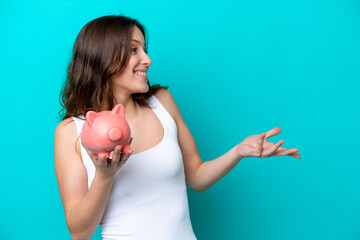 Young Caucasian woman holding a piggybank isolated on blue bakcground with surprise facial expression
