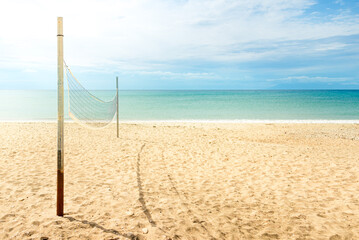 Beach volleyball net on a golden sand beach with turquoise sea waters and bright blue sunny sky