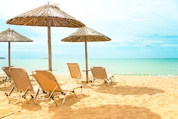 Straw umbrellas and sunbeds on a sunny golden beach seashore.
