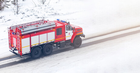 A red fire truck or Fire engine drives down a snowy street in winter to extinguish a fire and rescue people.