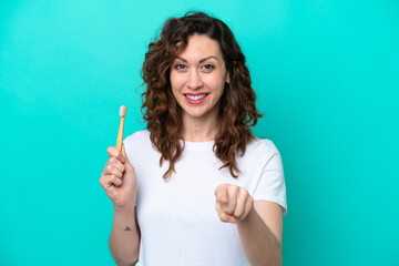 Young caucasian woman brushing teeth isolated on blue background points finger at you with a confident expression