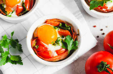 Baked Eggs with Bacon, Tomatoes, Spinach and Herbs on Bright Background, Healthy Breakfast or Snack