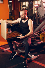 A young man with a beard with a happy face opens a pizza box in the gym