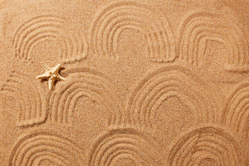 A pattern in the form of waves on the sand on the beach and a starfish. Natural background.