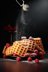 Belgian waffles with raspberries sprinkled with powdered sugar.