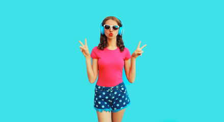 Portrait of cool teenager girl in headphones listening to music blowing her lips sending air kiss...