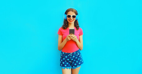 Portrait of happy smiling young woman in headphones listening to music with smartphone on blue background
