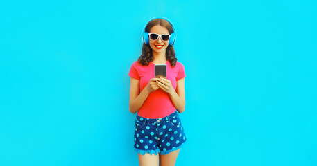 Portrait of happy smiling young woman in headphones listening to music with smartphone on blue...