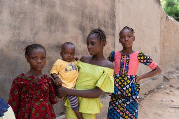 Group of young african girls with a baby boy posing in front of a wall - concept of human population overshoot