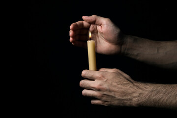 Male hands hold a burning candle on a black background