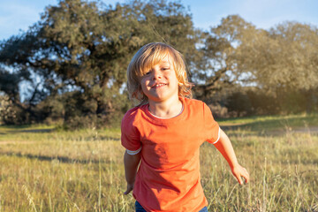 Happy little boy with blonde hair in field smiling, sunny day, outdoors. 