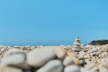 Fototapeta na wymiar Pyramid stones balance on the beach against a blue bright sky. Object in focus, blurred background, idea of a vacation or retweet by the sea