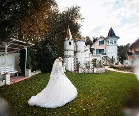 A stylish bride in a white wedding dress with a bouquet in her hands walks through the park with fabulous architecture. Image for your creative design or illustrations.
