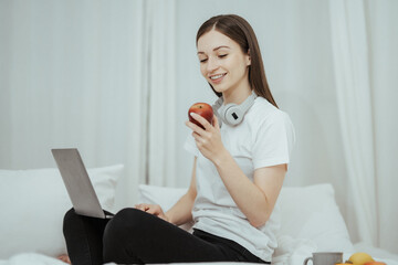 Happy woman holding apple and listening to music sitting on sofa in living room at home