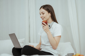 Happy woman holding apple and listening to music sitting on sofa in living room at home