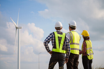 Back view of three engineers discussing and checking turbines on wind turbine farm. Renewable...