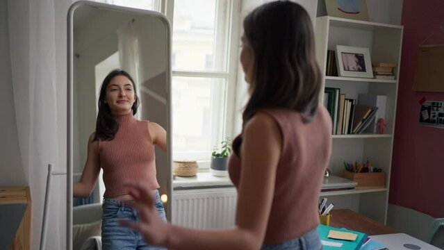Young teenage girl looking in the mirror in her room, trying on clothes and dancing.