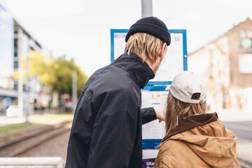 Woman and man orientating self on the public transport map on the street on bus station. Tourist looks at maps with public transport. Traveler looking for a way to the subway map. Search transport